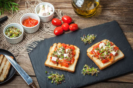 Grilled toasted bread with roasted tomatoes, feta cheese and radish sprouts.の写真素材
