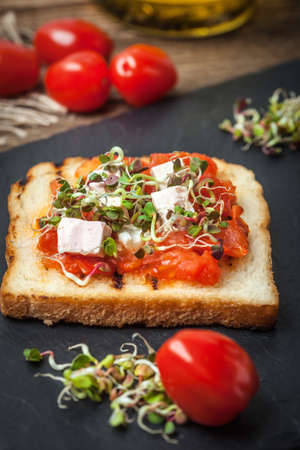 Grilled toasted bread with roasted tomatoes, feta cheese and radish sprouts.の写真素材