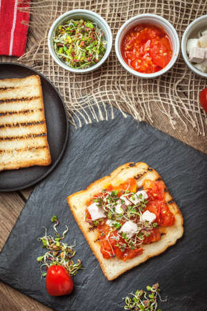 Grilled toasted bread with roasted tomatoes, feta cheese and radish sprouts.の写真素材