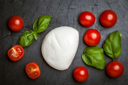 Mozzarella, tomato and basil on a dark gray stone.