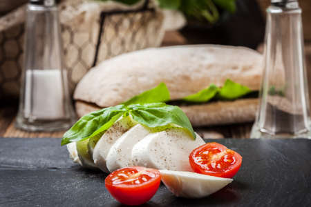 Mozzarella, tomato and basil on a dark gray stone.