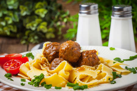 Tagliatelle, meatballs in dark sauce and tomato on a wooden background. Selective focus.の写真素材