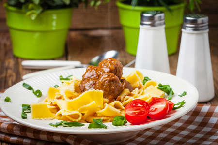 Tagliatelle, meatballs in dark sauce and tomato on a wooden background. Selective focus.の写真素材