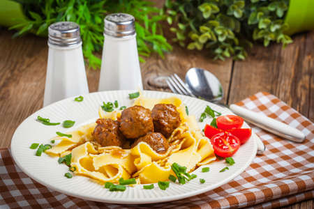 Tagliatelle, meatballs in dark sauce and tomato on a wooden background. Selective focus.の写真素材