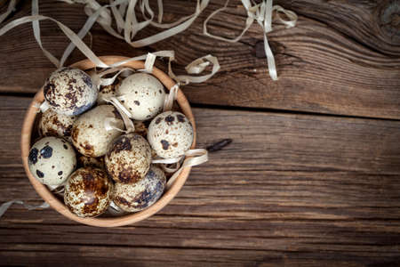 Raw quail eggs in a wooden bowl on wooden table. Selective focus.の写真素材