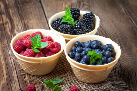Blackberries, raspberries and blueberries in a waffle bowls on a wooden table. Selective focus.