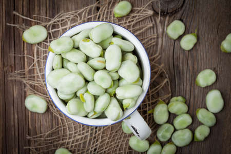 Fresh broad beans in a container on a wooden table. Selective focus. Top view.