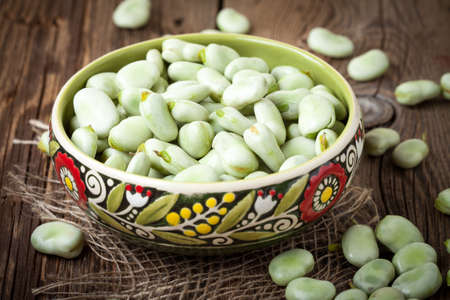 Fresh broad beans in a container on a wooden table. Selective focus.の写真素材