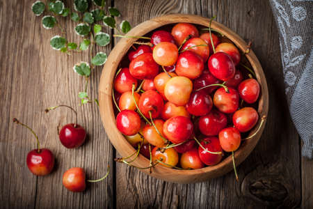 Freshly harvested cherries in a wooden bowl. Top view. Dark light.の写真素材