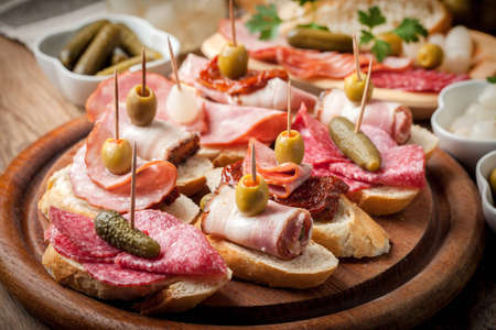 Spanish cuisine. Tapas with sliced sausage, bacon, salami, olives, dried tomatoes and parsley on a wooden table.の写真素材