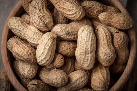Top view of dried peanuts in wooden bowl.