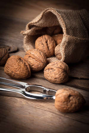 Walnuts in burlap bag on old wood table. Dark light.