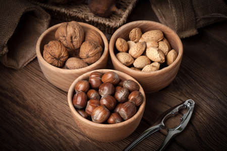 Walnuts, hazelnuts and almonds in-shell in wooden bowl on old wood table. Dark light.