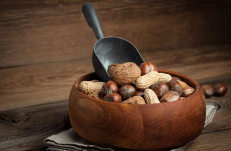 Walnuts, hazelnuts and peanuts in wooden bowl on old wood table. Dark light.の写真素材