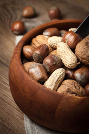 Walnuts, hazelnuts and peanuts in wooden bowl on old wood table. Dark light.