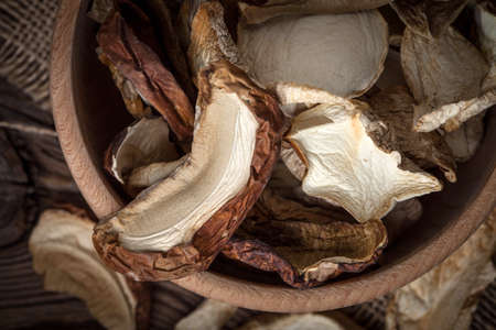 Dried mushrooms in wooden bowl on dark background. Top view.の写真素材