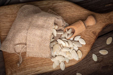 Pumpkin seeds in a sack and spoon on the wooden table.  Dark light.の写真素材