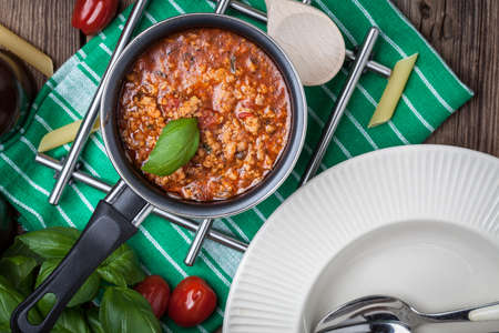 Pasta, bolognese sauce and basil on wooden table. Top view.