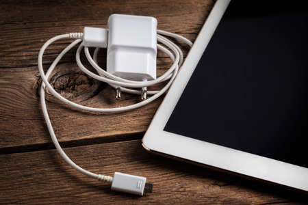 Digital table computer and a charger on wood background.の写真素材