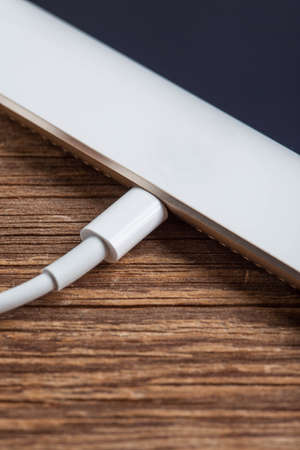 A smartphone is charging with power bank on a wood board.