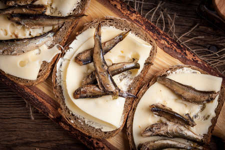 Sandwich with sprats and cheese on wooden cutting board.の写真素材