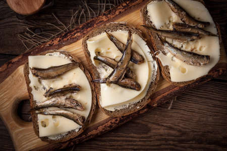 Sandwich with sprats and cheese on wooden cutting board.の写真素材