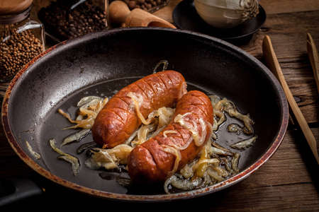 Fried sausage with onions in a frying pan.の写真素材