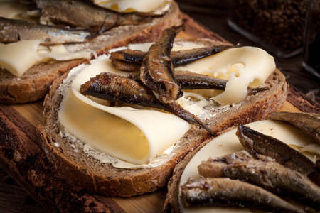 Sandwich with sprats and cheese on wooden cutting board.の写真素材