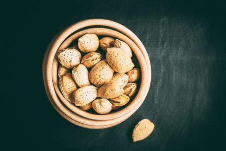 Almonds in a wooden bowl on a dark background. Dark light.