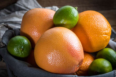 Fresh juicy citrus fruits in a basket on a wooden background.の写真素材