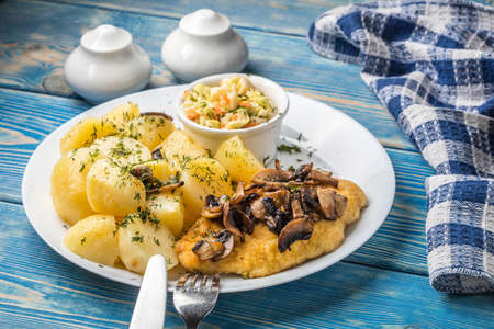 Fried chicken breast served with mushrooms and potatoes.