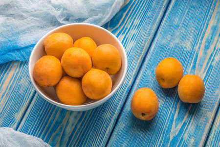 Bowl full of fresh apricots on a blue wooden table.の写真素材