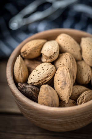 Almonds in-shell in wooden bowl on old wood table.の写真素材