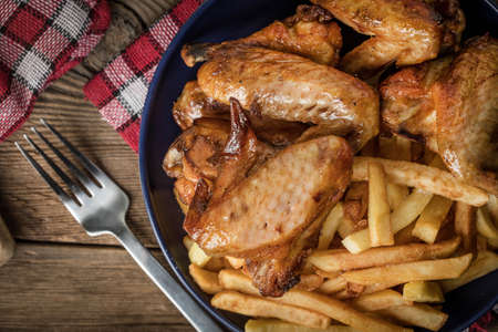 Baked chicken wings with french fries on wooden table. Top view.の写真素材