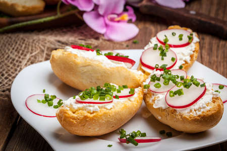 Toasts with radish, chives and cottage cheese on a wooden table. Tasty snack. Selective focus.の写真素材