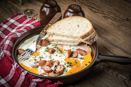 Tasty cooked egg with chopped sausages in pan.の写真素材