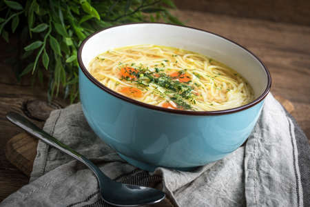 Broth - chicken soup with noodles in a blue bowl.の写真素材
