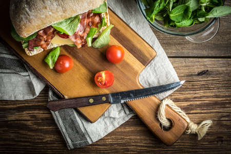 Ciabatta sandwich with arugula salad, bacon and yellow cheese on wooden board. Top view.の写真素材