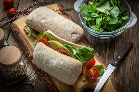 Ciabatta sandwich with arugula salad, bacon and yellow cheese on wooden board.の写真素材