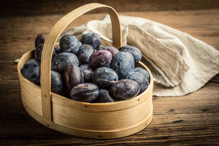 Garden plums in basket on wooden table.
