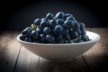 Dark grape in bowl on wooden table. Selective focus.の写真素材