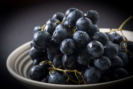 Dark grape in bowl on wooden table. Selective focus.の写真素材