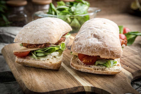 Ciabatta sandwich with arugula salad, bacon and yellow cheese on wooden board.の写真素材