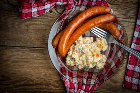 Thin sausages served with vegetable salad on a wooden table. Top view.