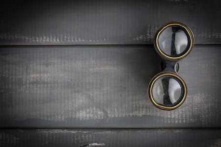 Old binoculars covered with patina on a gray woodenbackground.