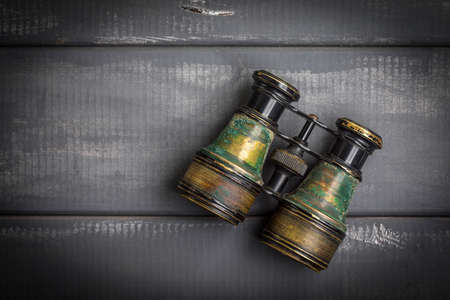Old binoculars covered with patina on a gray woodenbackground.の写真素材