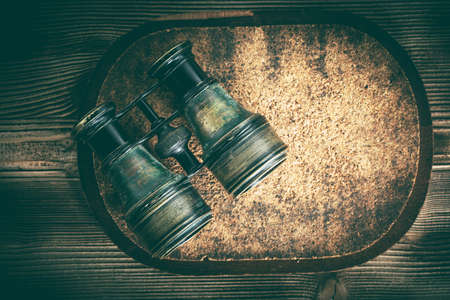Old binoculars covered with patina on wooden background.の写真素材
