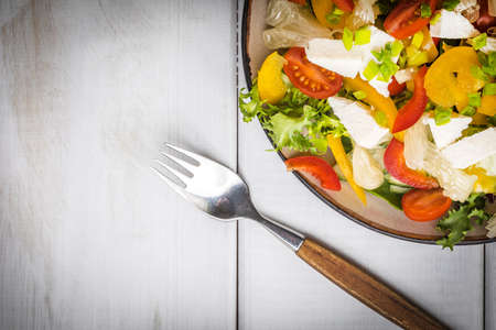 Salad with cheese and fresh vegetables on white wooden table.の写真素材