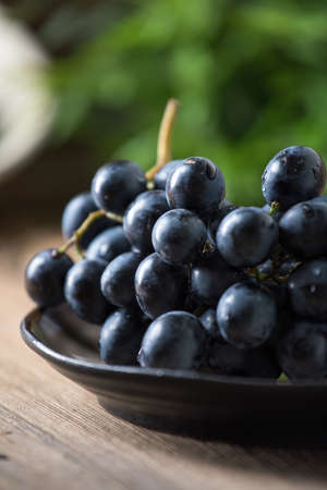 Dark grape in bowl on wooden table. Selective focus.の写真素材