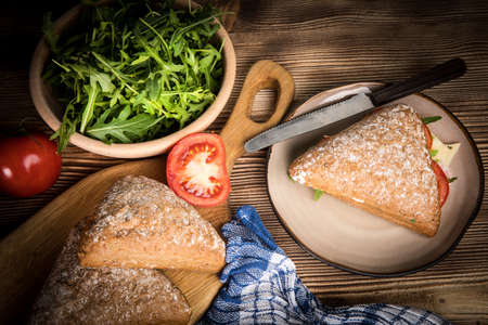 Triangular sandwich with cheese, ham and tomato on a wooden table.の写真素材